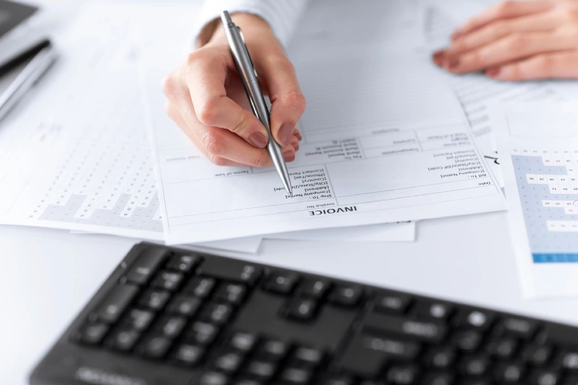 A person writing on paper next to a keyboard.