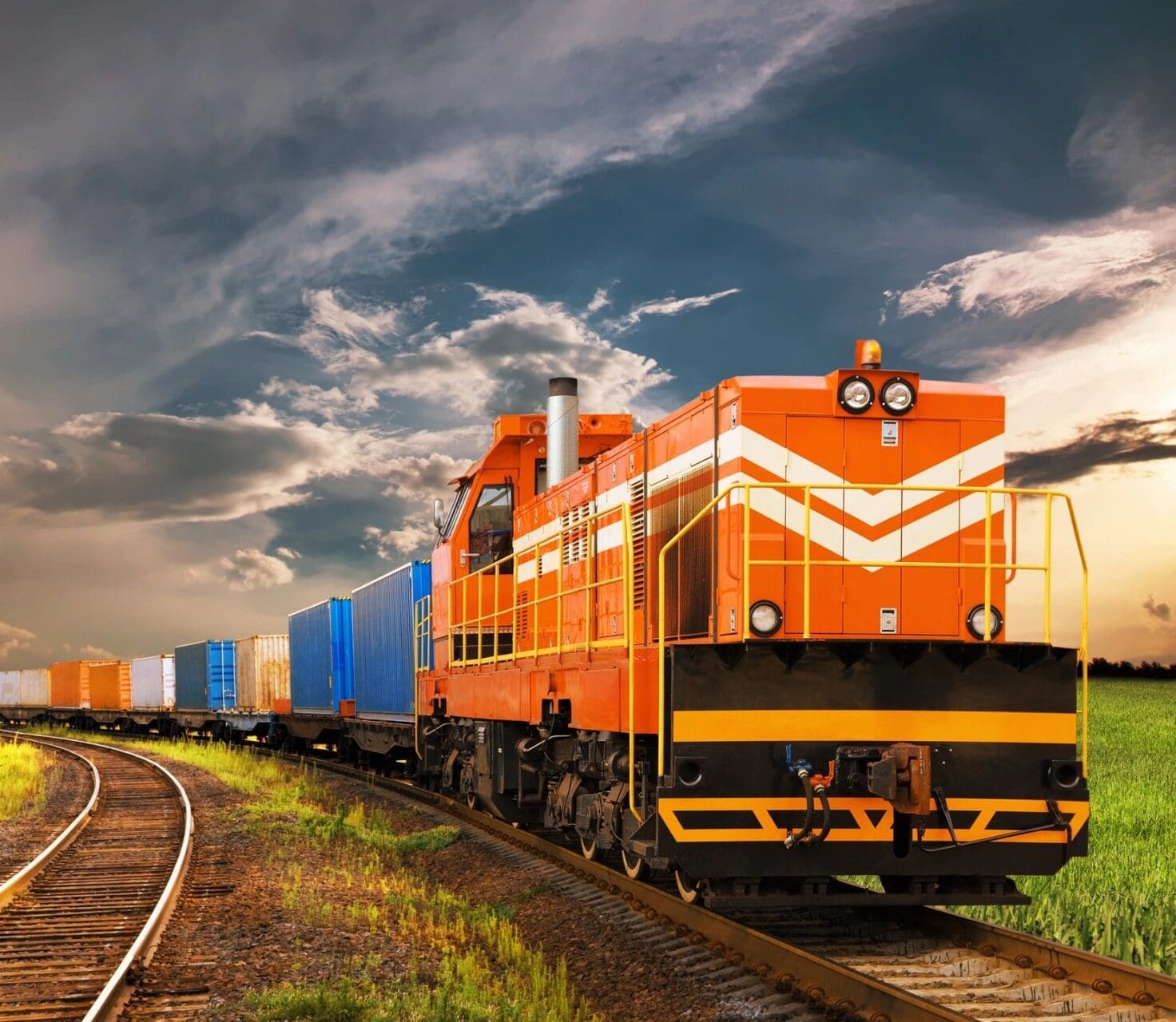 A train is traveling down the tracks under a cloudy sky.